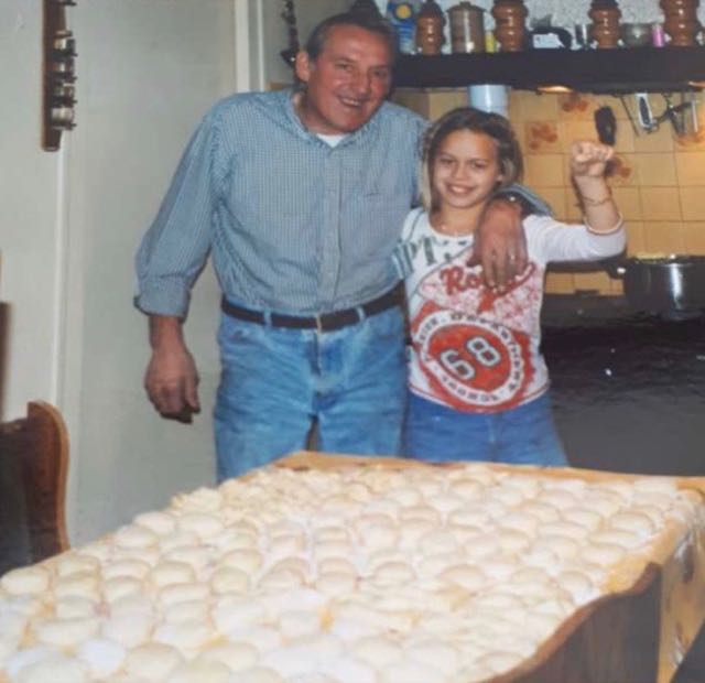 Photo de famille : un homme et une petite fille sourient dans une cuisine, derrière une grande table couverte de petites boules de pâte.
